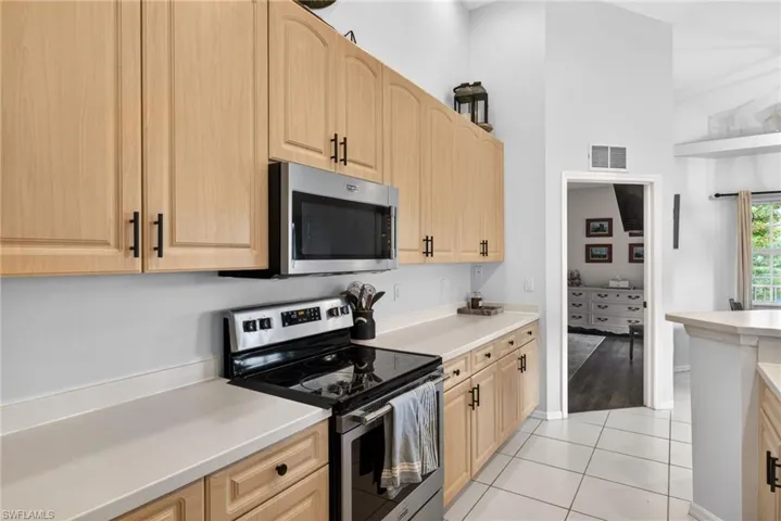 Kitchen featuring light wood cabinetry with dark hardware, stainless steel appliances including an oven and microwave, light-toned countertops, and tile flooring
