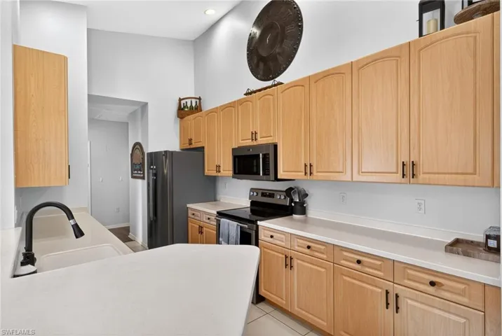 Kitchen featuring light wood cabinetry, white countertops, stainless steel appliances, a built-in microwave, and a black gooseneck faucet