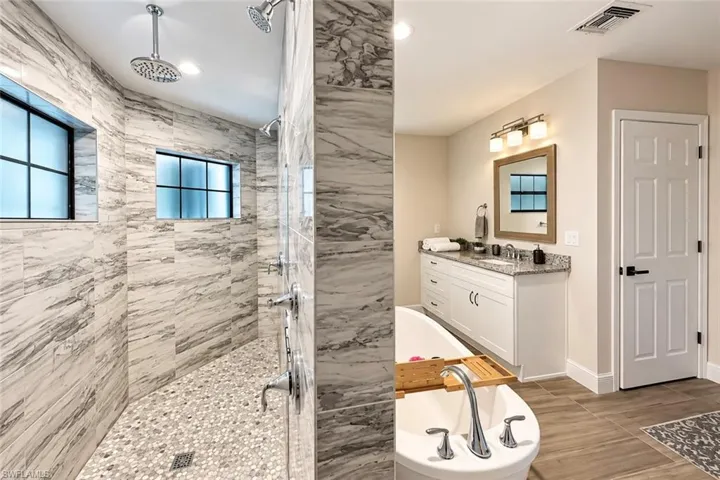 Walk-in shower with natural stone tile walls and pebble floor, dual shower heads, and recessed windows