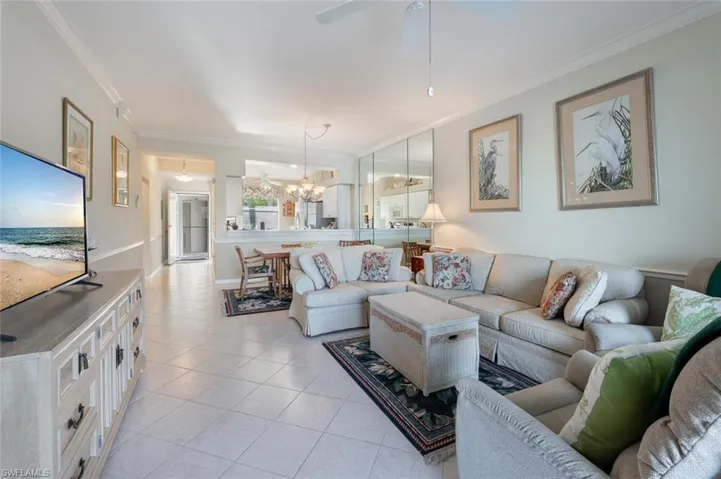 Living area featuring light tile patterned floors, ceiling fan with notable chandelier, and ornamental molding