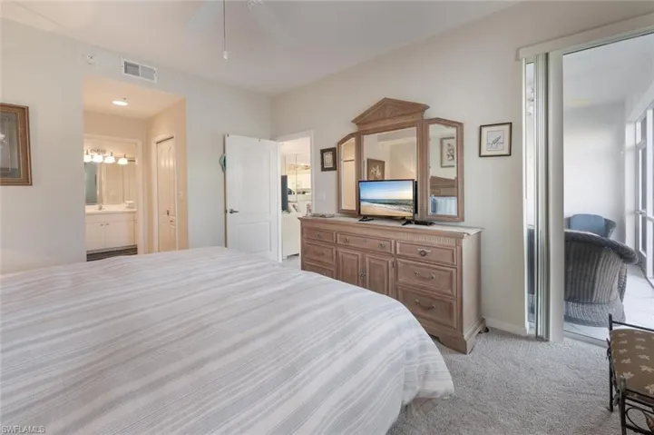 Bedroom with visible vents, light colored carpet, connected bathroom, and a ceiling fan