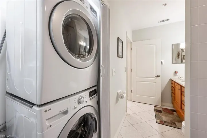 Washroom with visible vents, baseboards, laundry area, light tile patterned flooring, and stacked washer / drying machine