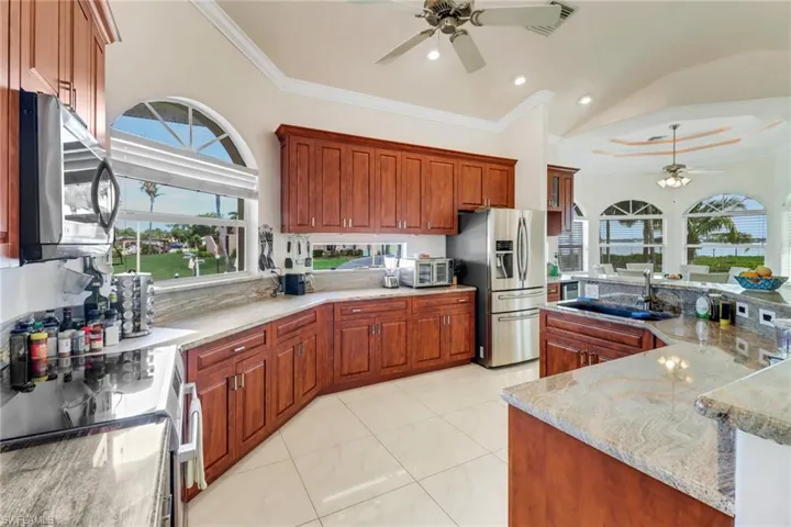 Kitchen featuring appliances with stainless steel finishes, ornamental molding, a sink, ceiling fan, and light stone countertops