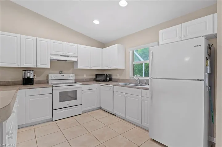 Kitchen featuring white appliances, lofted ceiling, white cabinetry, light tile patterned floors, and sink