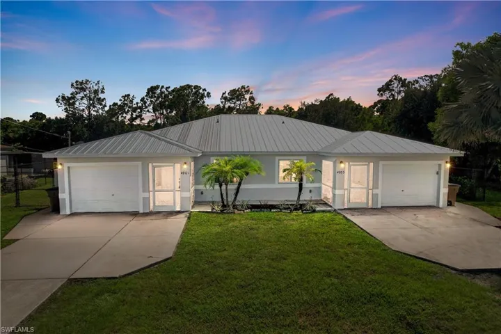 Exterior featuring a metal roof, attached garages, paved driveways, and established landscaping