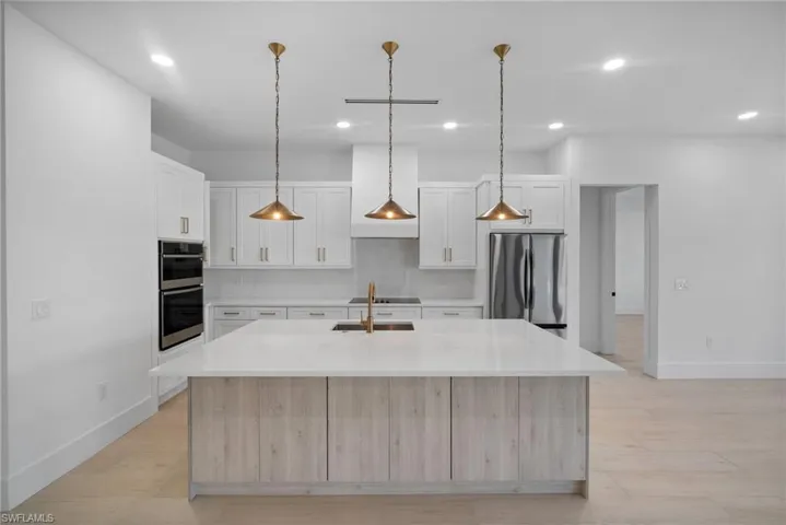 Kitchen with a center island with sink, light wood-type flooring, appliances with stainless steel finishes, decorative light fixtures, and white cabinetry