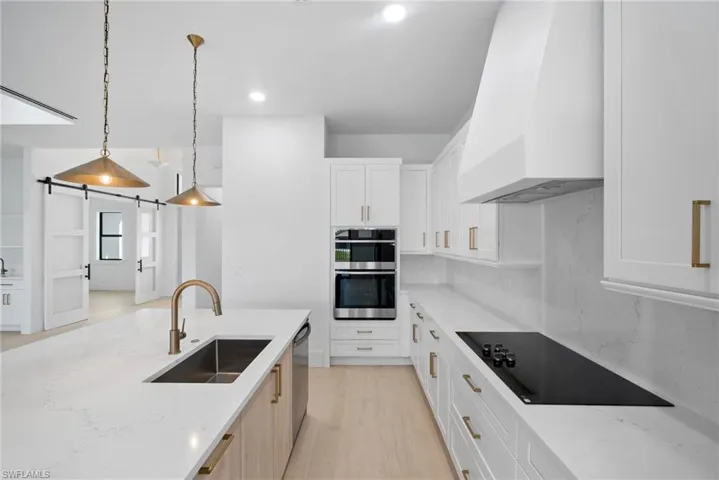 Kitchen featuring sink, stainless steel appliances, a barn door, pendant lighting, and custom exhaust hood