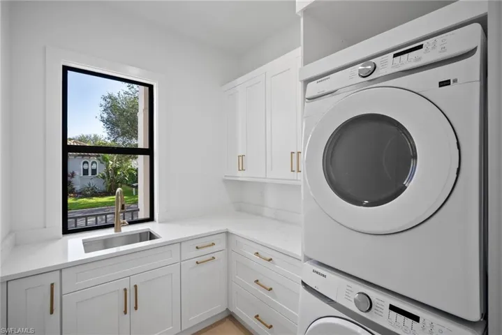 Laundry area featuring cabinets, stacked washing maching and dryer, and sink