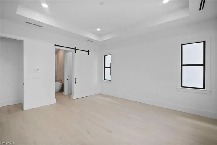 Unfurnished bedroom featuring a raised ceiling, a barn door, ensuite bathroom, and light hardwood / wood-style floors