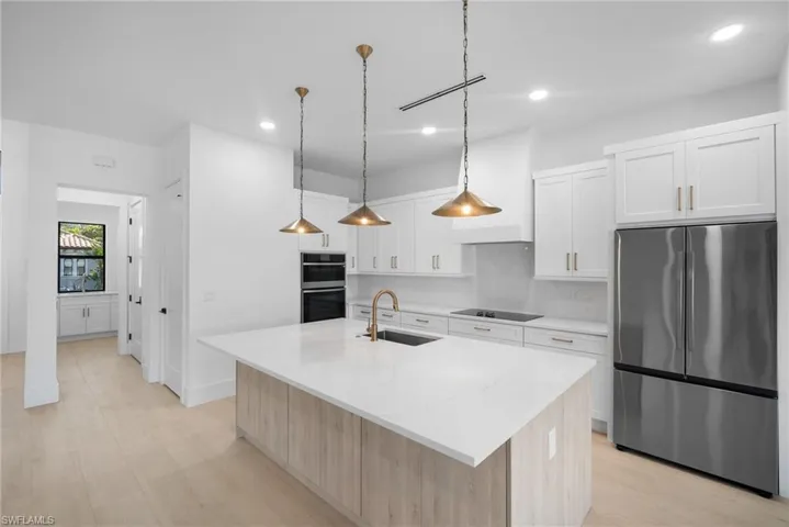 Kitchen featuring sink, hanging light fixtures, stainless steel appliances, an island with sink, and white cabinets