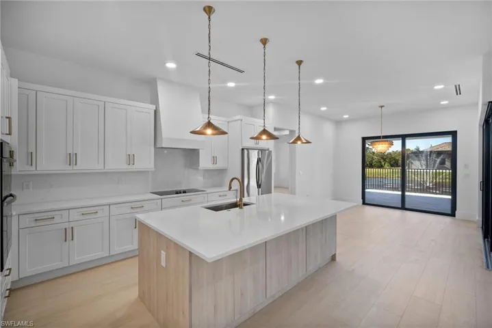 Kitchen featuring a kitchen island with sink, sink, hanging light fixtures, stainless steel fridge, and white cabinetry