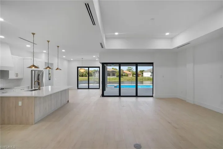 Kitchen featuring light wood-type flooring, a spacious island, decorative light fixtures, white cabinets, and stainless steel refrigerator