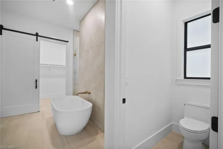 Bathroom featuring hardwood / wood-style flooring, toilet, and a tub to relax in
