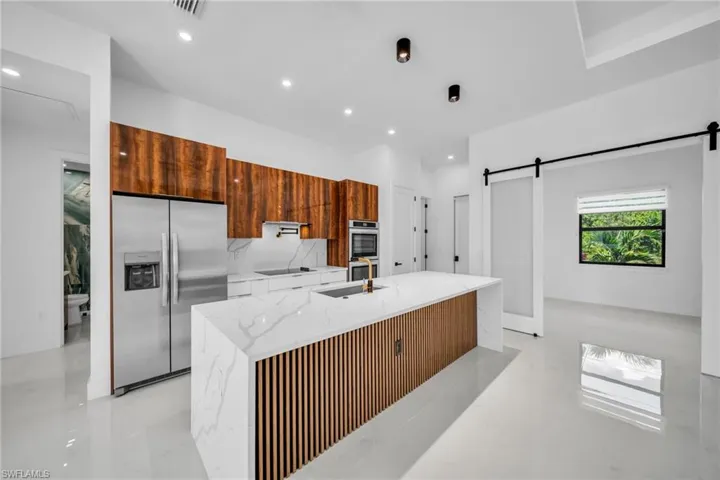 Kitchen with appliances with stainless steel finishes, modern cabinets, light stone countertops, brown cabinetry, and a kitchen island with sink