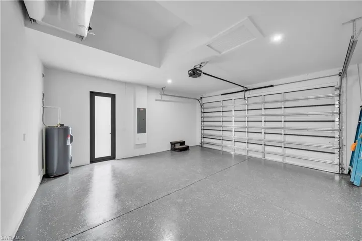 Garage featuring water heater, electric panel, and a garage door opener