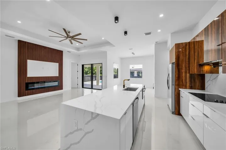 Kitchen with modern cabinets, light stone countertops, a large island with sink, open floor plan, and a glass covered fireplace
