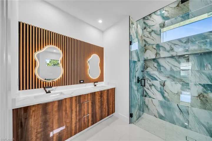 Bathroom with a marble finish shower, double vanity, and recessed lighting
