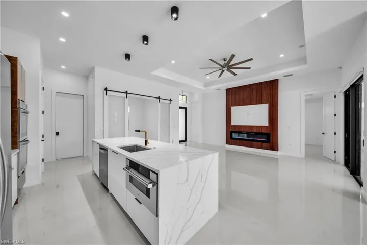 Kitchen with modern cabinets, white cabinets, a barn door, an island with sink, and light stone countertops