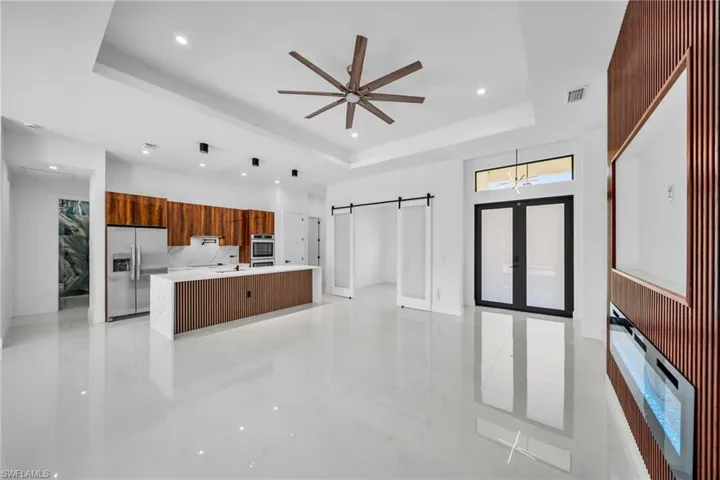 Kitchen featuring a raised ceiling, a barn door, modern cabinets, a large island with sink, and stainless steel refrigerator with ice dispenser