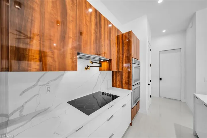 Kitchen with modern cabinets, tasteful backsplash, brown cabinets, light stone countertops, and recessed lighting
