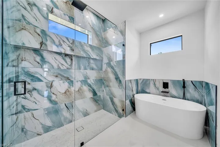 Full bath featuring tile walls, a marble finish shower, a freestanding tub, wainscoting, and marble finish floors