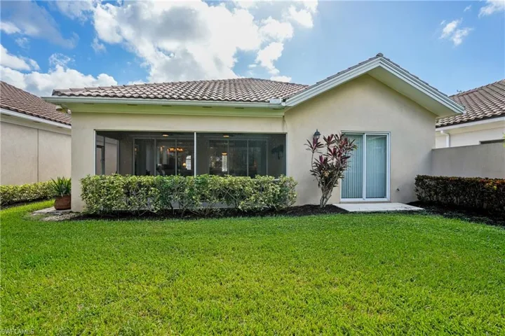 Rear view of house featuring a yard, stucco siding, a tiled roof, and a sunroom