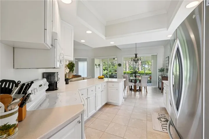 Kitchen featuring white appliances, recessed lighting, a peninsula, white cabinetry, and hanging light fixtures