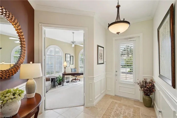 Entrance foyer with crown molding, light carpet, wainscoting, and light tile patterned floors