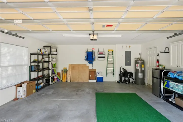 Garage with electric panel, freestanding refrigerator, electric water heater, and a garage door opener