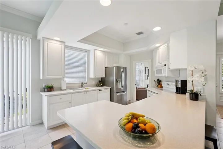 Kitchen featuring a peninsula, a breakfast bar, crown molding, light countertops, and white cabinetry