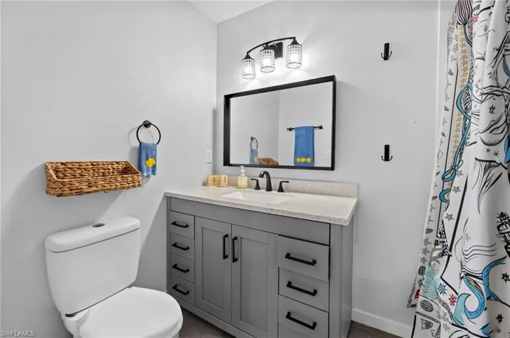 Bathroom featuring a grey vanity with a light-toned countertop, a rectangular mirror, and a three-light fixture