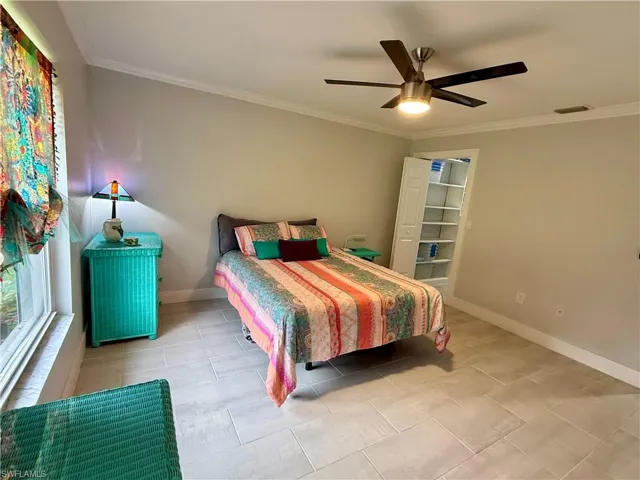 Spacious room featuring vaulted ceilings, crown molding, light-toned tile flooring, a ceiling fan with integrated lighting, and a bi-fold door closet with built-in shelving