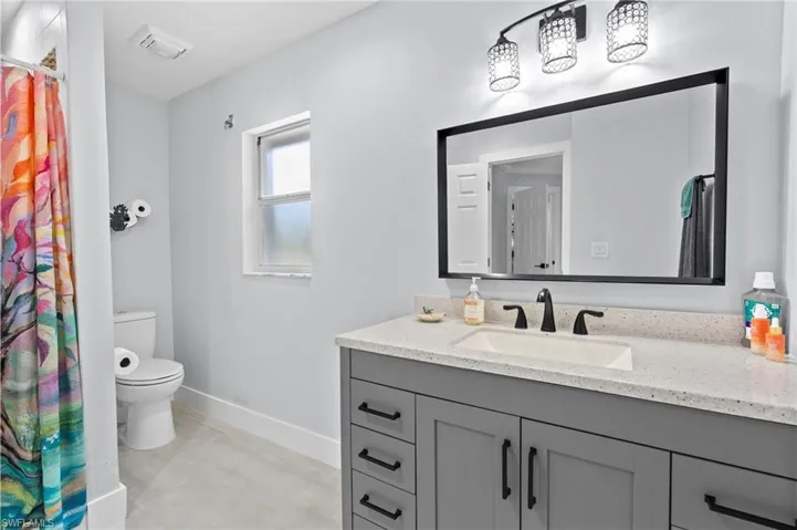 Bathroom featuring a single vanity with a solid surface countertop, undermount sink, and matte black faucet