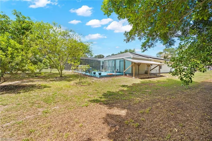 Expansive backyard featuring mature trees, a screened-in lanai with a blue-painted concrete patio, and a covered outdoor structure