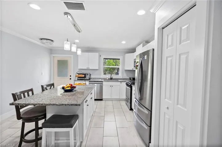 Kitchen with a large island featuring a speckled countertop, white cabinetry, stainless steel appliances, and tiled flooring