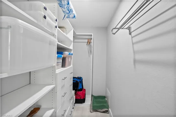 Walk-in closet featuring custom white shelving, built-in drawers with modern pulls, and a wall-mounted drying rack