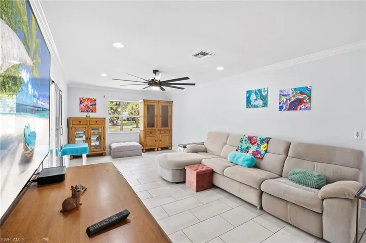 Spacious living area featuring light-toned tile flooring, recessed lighting, and crown molding