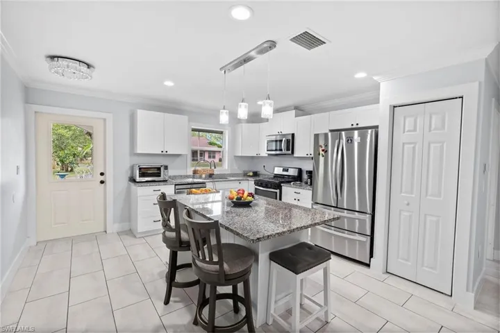 Contemporary kitchen featuring a granite-topped island with pendant lighting, white cabinetry, stainless steel appliances, and large format tile flooring