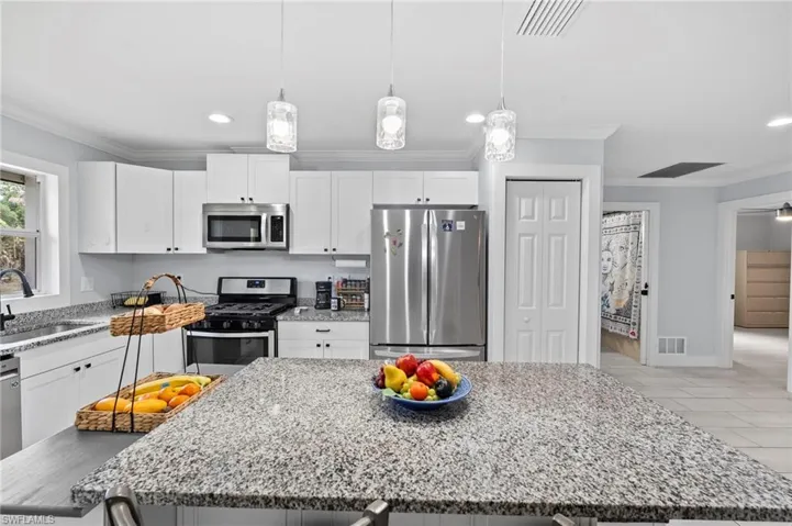 Kitchen featuring a granite-topped island, white cabinetry, and stainless steel appliances