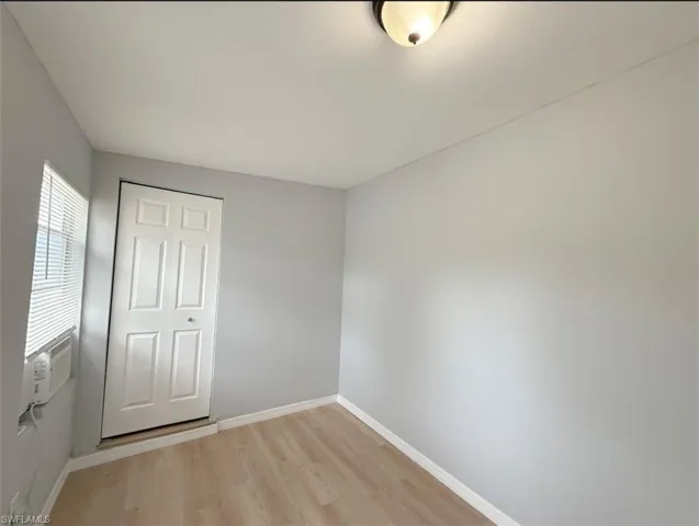 Unfurnished bedroom with cooling unit, a closet, baseboards, and light wood-type flooring
