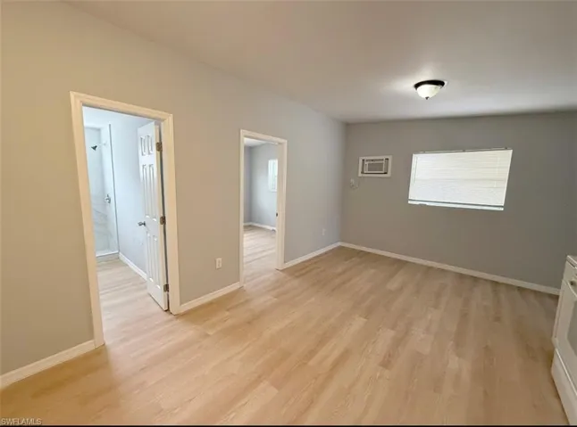 Spare room with baseboards, an AC wall unit, and light wood-type flooring