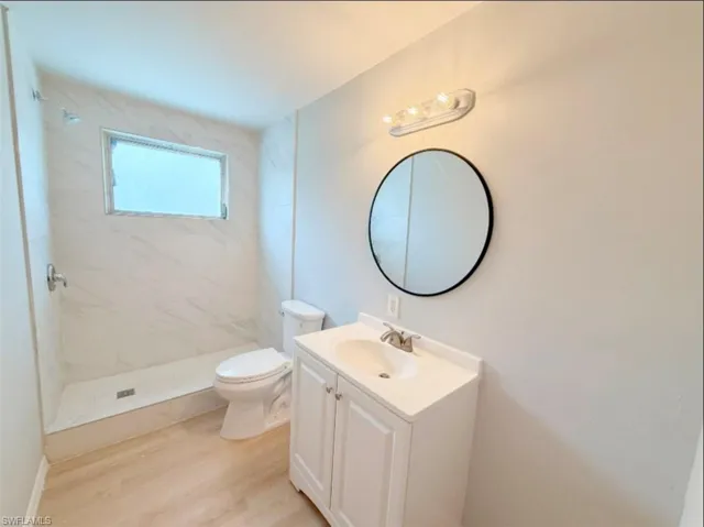 Full bathroom featuring a marble finish shower, toilet, vanity, and wood finished floors