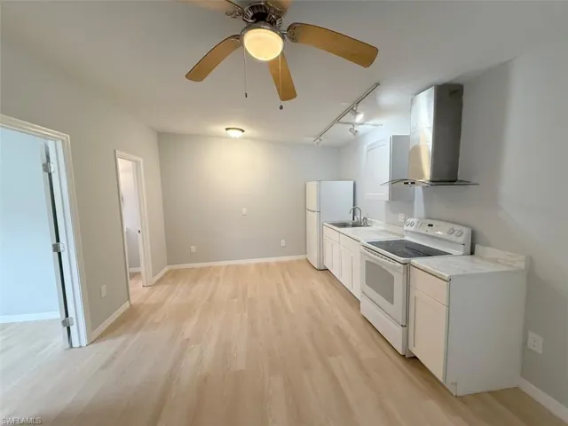 Kitchen featuring light countertops, a sink, wall chimney exhaust hood, light wood-style flooring, and white appliances