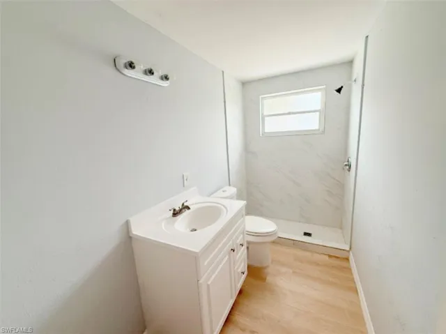 Full bath with baseboards, toilet, wood finished floors, vanity, and a stall shower