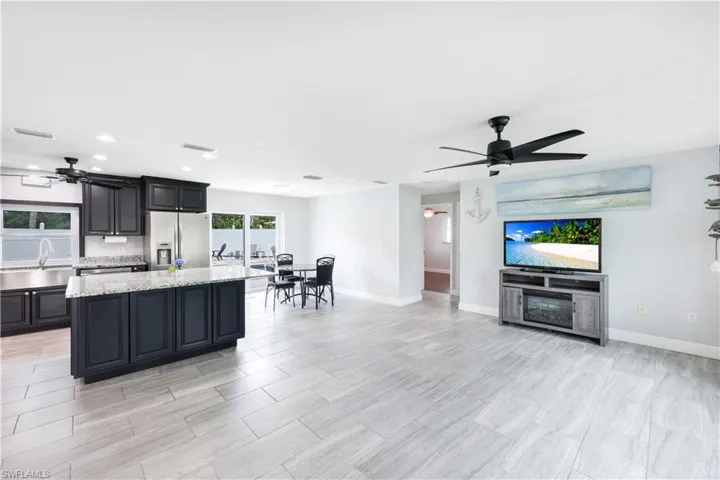 Kitchen featuring white refrigerator with ice dispenser, light stone countertops, a kitchen island, ceiling fan, and sink