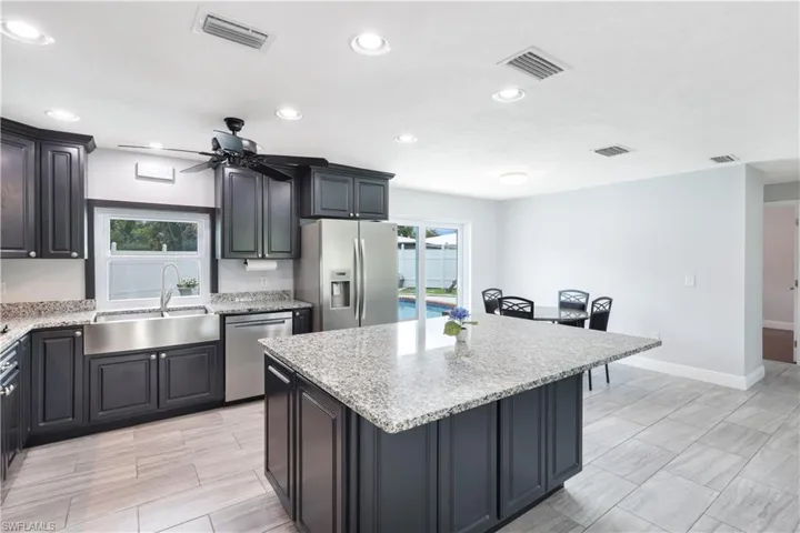 Kitchen featuring stainless steel appliances, light stone countertops, ceiling fan, sink, and a kitchen island