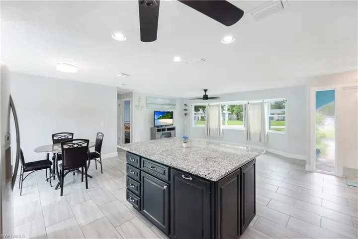 Kitchen with ceiling fan, light stone counters, a center island, and light tile patterned floors