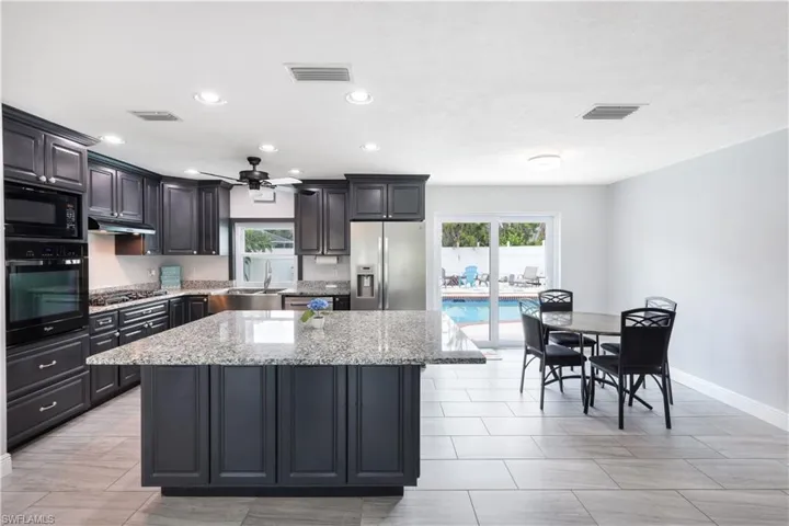 Kitchen featuring black appliances, a kitchen island, plenty of natural light, and light stone countertops