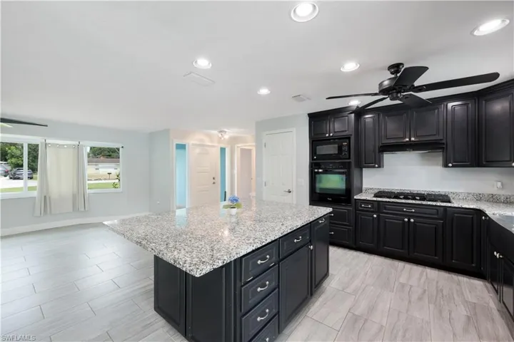 Kitchen featuring black appliances, a center island, light stone countertops, and ceiling fan