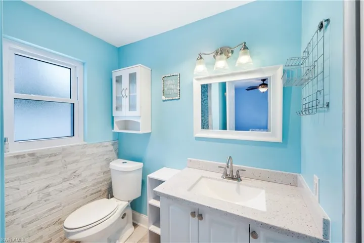 Bathroom featuring tile walls, toilet, vanity, and ceiling fan